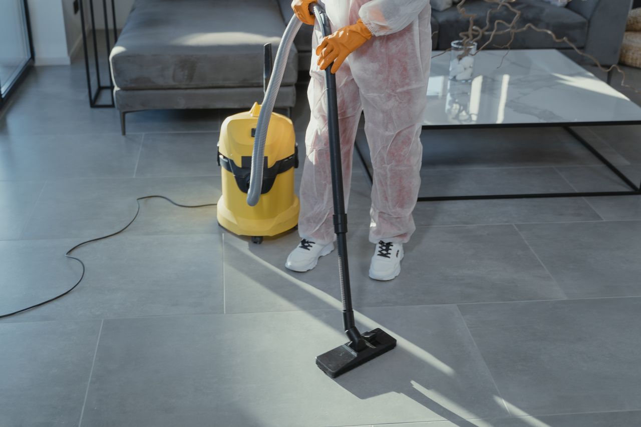 services-04 A professional cleaner in protective gear vacuuming the floor in a modern living room.