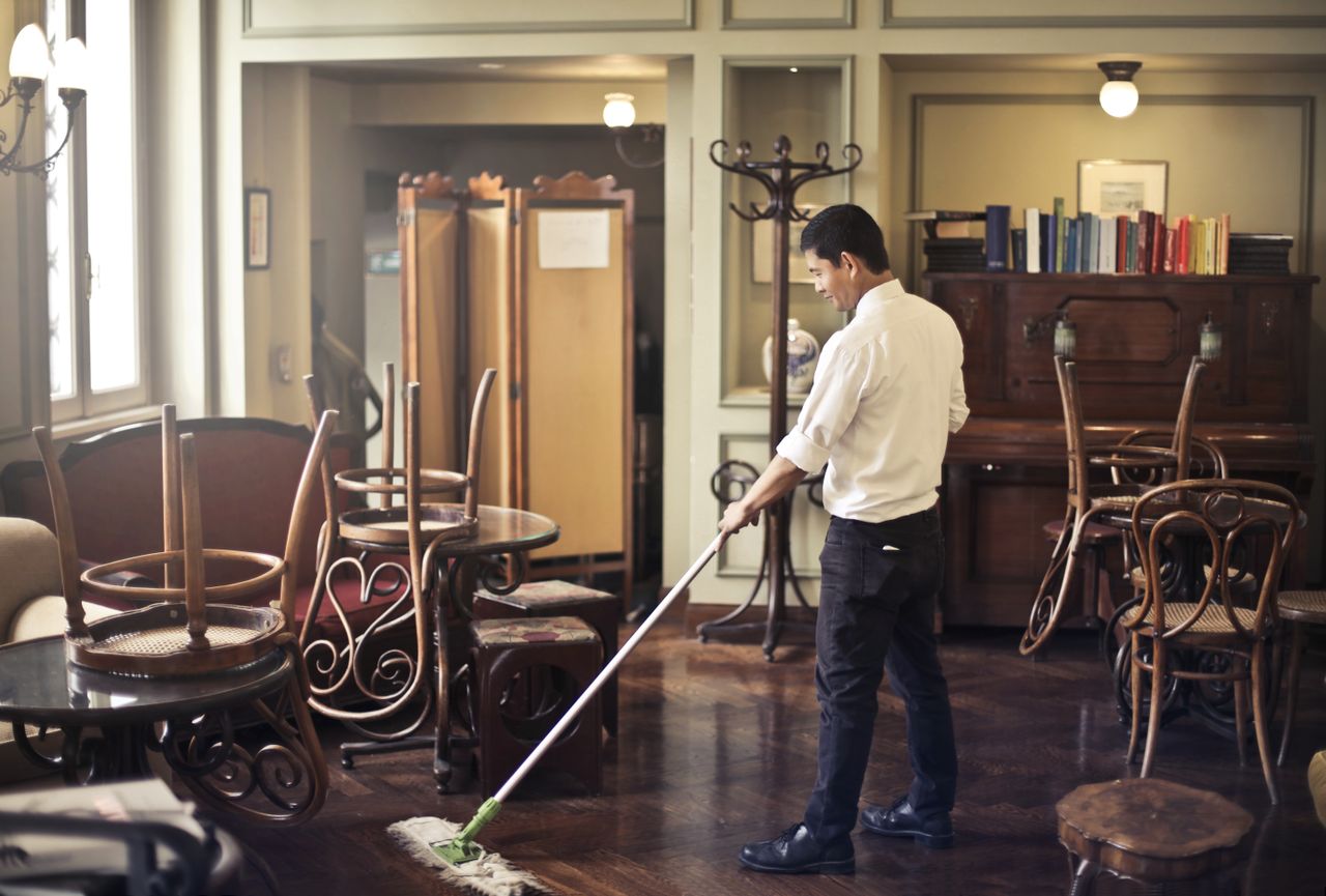 about-us-01 Side view of young ethnic male in uniform cleaning floor with mop while working in retro styled restaurant
